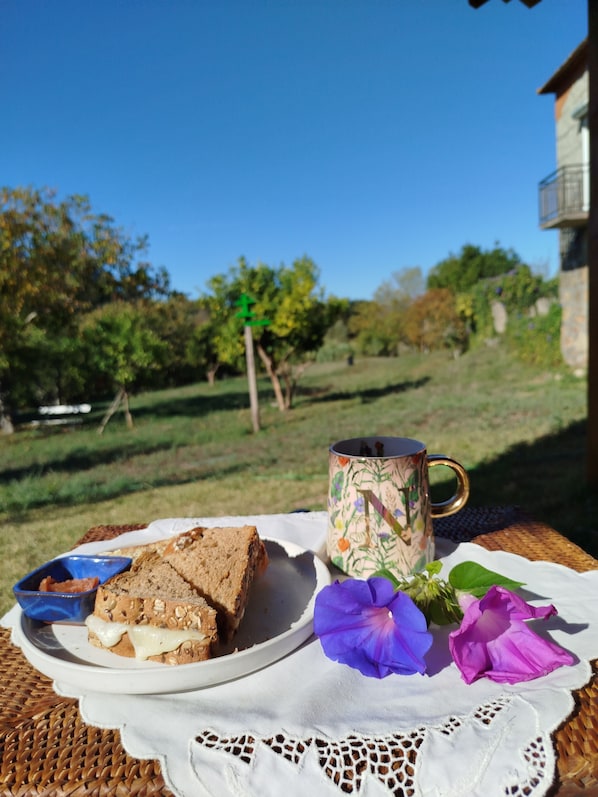 A table with a plate of sandwiches, a mug, and flowers.