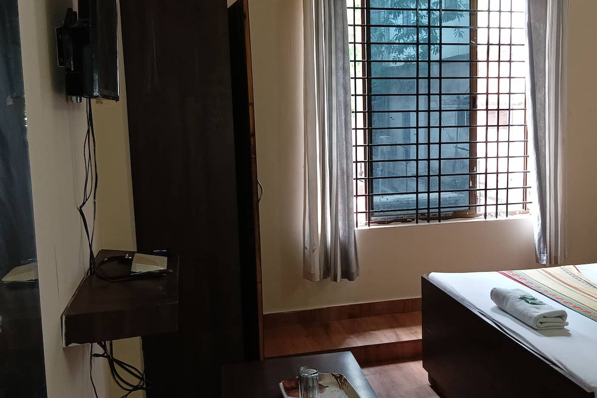 Quarto de hotel com uma cama, uma escrivaninha, uma cadeira, uma TV fixada na parede e uma janela com vista para árvores.