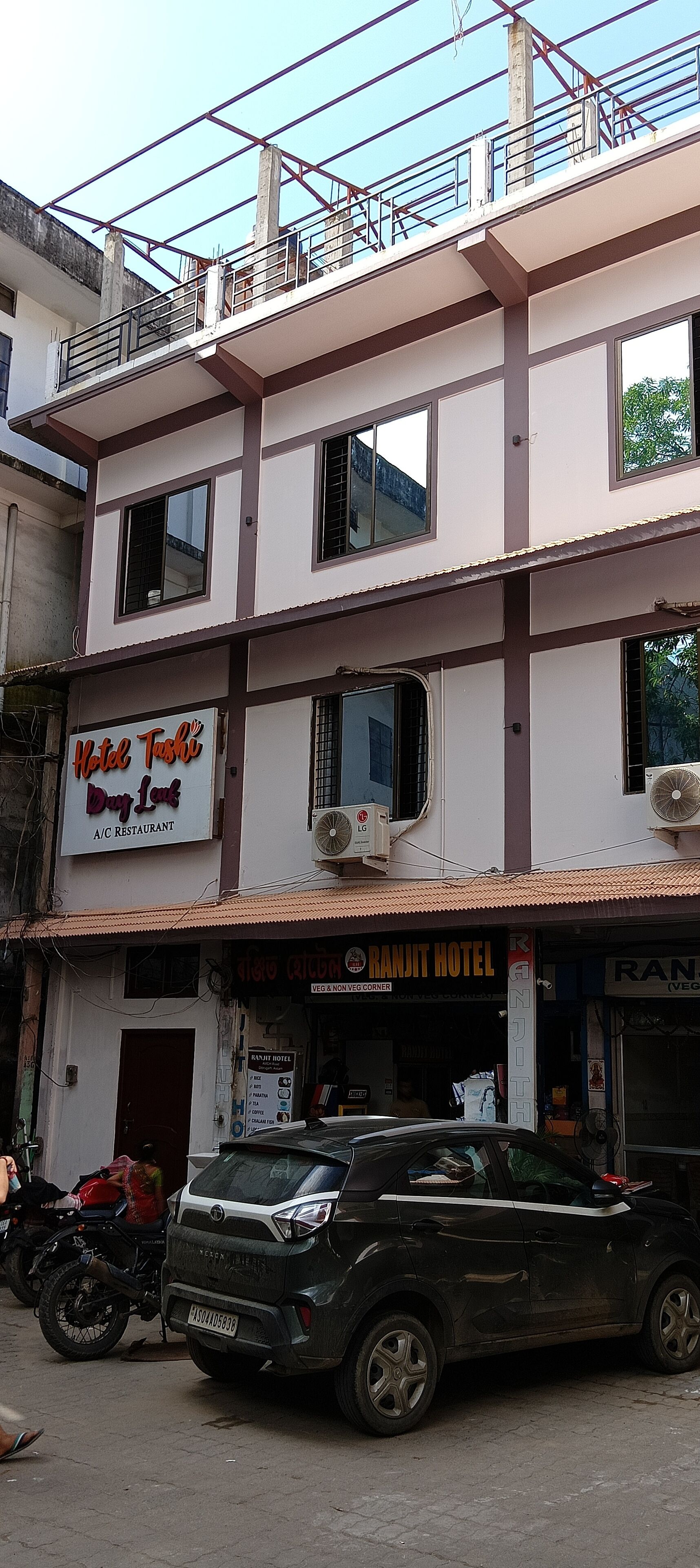 Ein mehrstöckiges Gebäude mit Schildern für 'Hotel Tashi Day Inn' und 'Ranjit Hotel', die ein Restaurant und ein Hotel anzeigen.