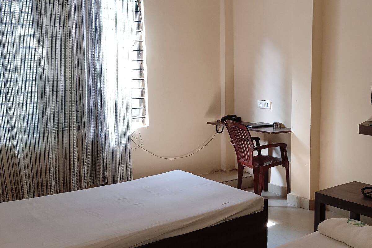Quarto de hotel com cama, escrivaninha com cadeira, televisão na parede e mesinha com bandeja.
