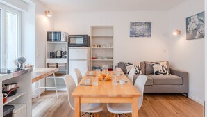 Una cocina moderna con microondas, horno y alacenas blancas. Hay una mesa de comedor con sillas y un sofá gris en la zona de estar.