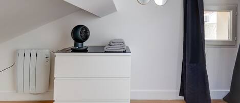 A modern room with a white chest of drawers, a black hairdryer, and a window with a black curtain.