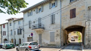 A narrow street with a building featuring a stone facade, a blue parking space, and a pedestrian archway. - L'Écrin de Beaucaire - Climatisé, à 30 min d'Arles (Beaucaire)