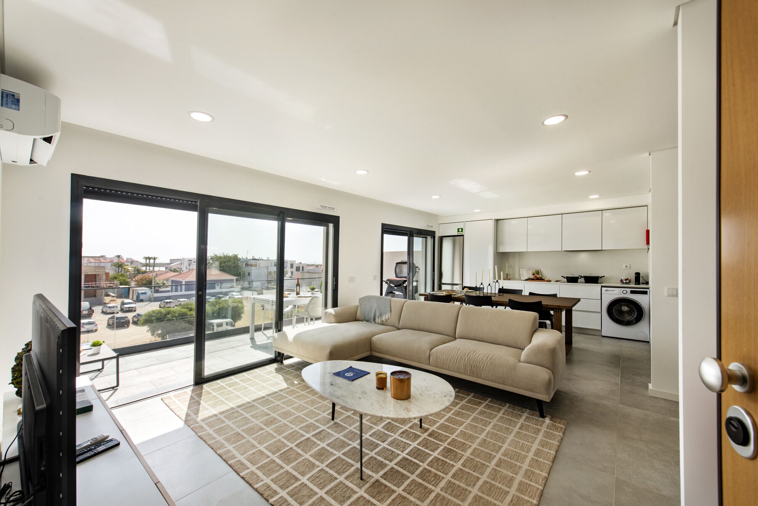 Een modern appartement met een zithoek, keuken en grote schuiframen naar een balkon.