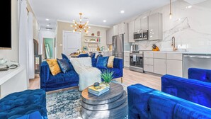 Una sala de estar moderna con un sofá azul, una mesa redonda de centro y una cocina al fondo.