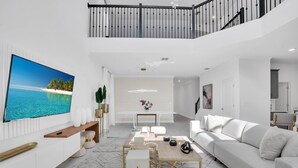 A modern living room with a large flat-screen TV, a white sofa, a wooden coffee table, and a dining area with a bench and chairs. - Batman | Mickey | Game Room | 4 Miles Disney 2669 (Kissimmee)