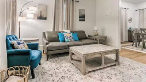 A living room with a sofa, armchairs, a coffee table, and a dining area in the background.