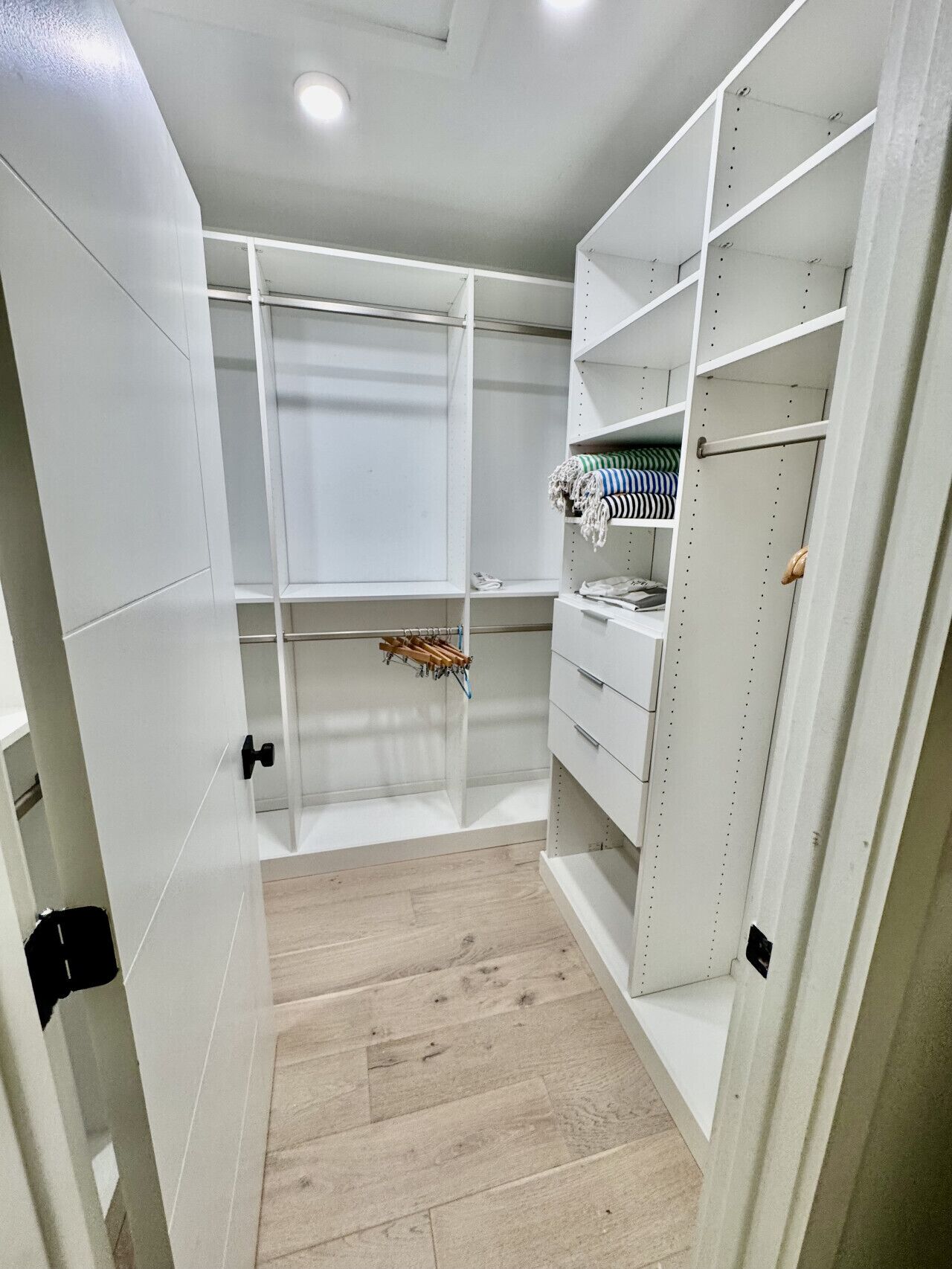 A walk-in closet with white shelving, a wooden floor, and a window.