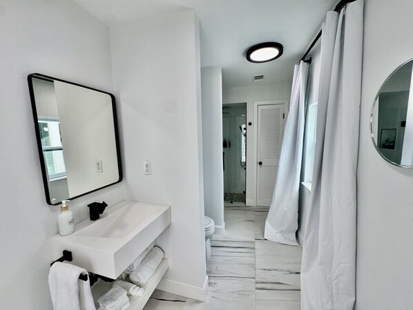 Une salle de bain moderne avec un lavabo blanc, un miroir et un rideau de douche.