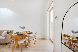 A modern living room with a dining area, featuring a round wooden table, matching chairs, and a large mirror. - The Sunny Duplex at BoaVista Flats (Porto)