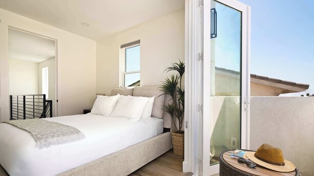 A bedroom with a bed, a potted plant, a wicker side table, and a sliding glass door leading to an outdoor area. - Coastal Ocean Beach Compound Escape (San Diego)