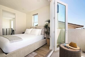 Un dormitorio con cama, una planta en maceta, una mesita de noche de mimbre y un ventanal corredero que da a un espacio exterior.
