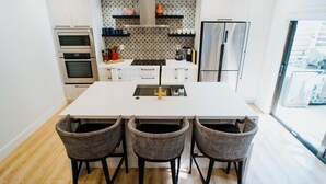 Een moderne keuken met een centraal eiland, inbouwovens, een koelkast en rieten barstoelen.