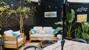 Een gezellig buiten zitgedeelte met rieten meubels, een houten tafel en potplanten.