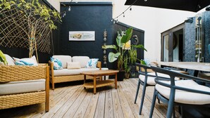 Een houten terras met een rieten bank, een houten tafel en stoelen.