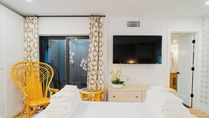 Hotelkamer met een bed, een aan de muur bevestigde televisie, een stoel, een tafeltje en een plant.