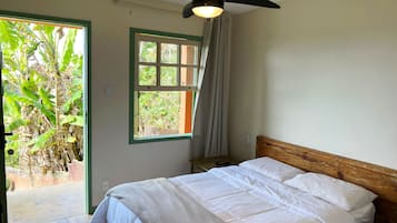 A bedroom with a bed, a ceiling fan, a window with curtains, and a view of greenery outside.