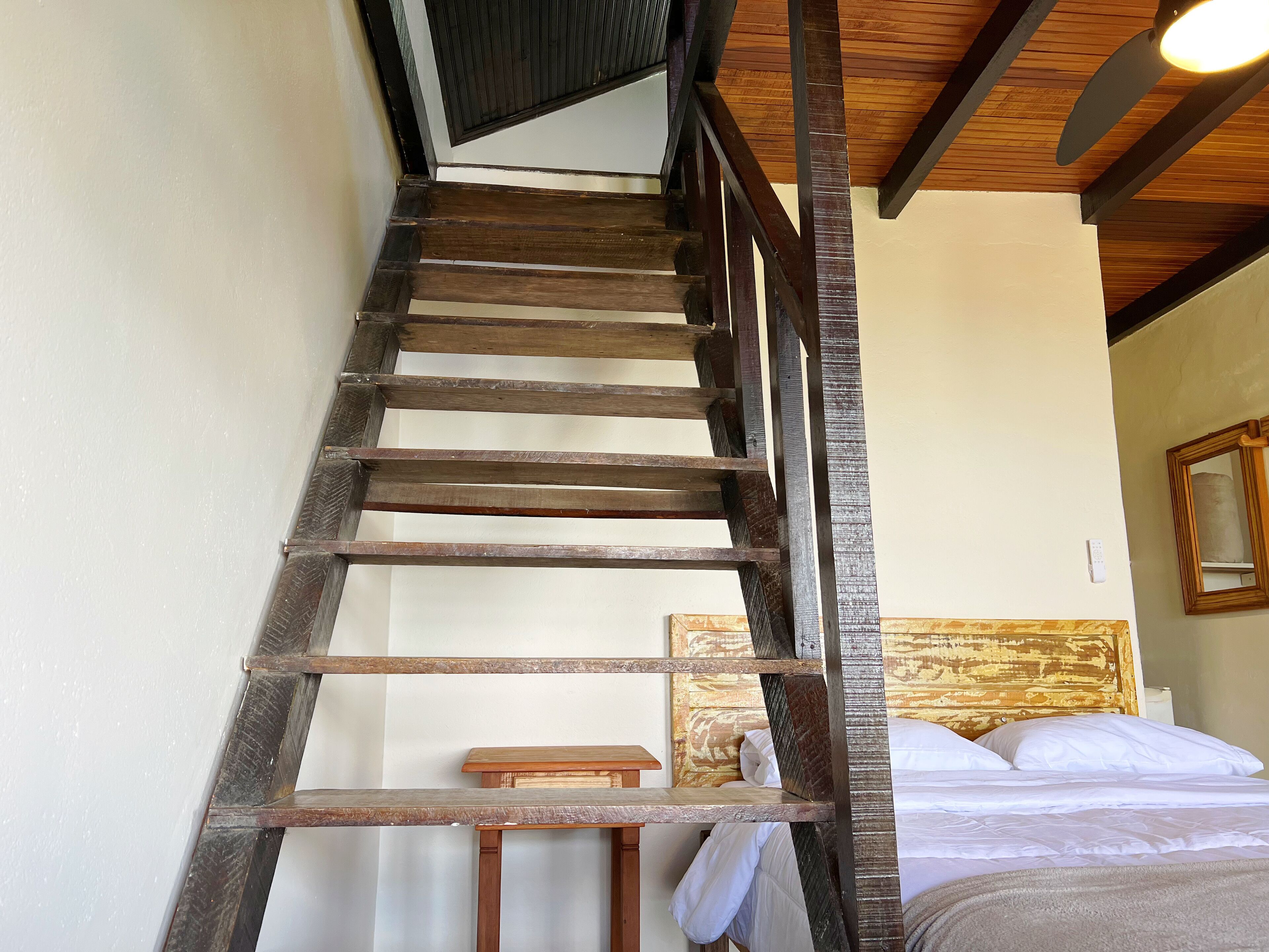 Una escalera de madera que conduce a un dormitorio con cama, almohadas y cabecera.