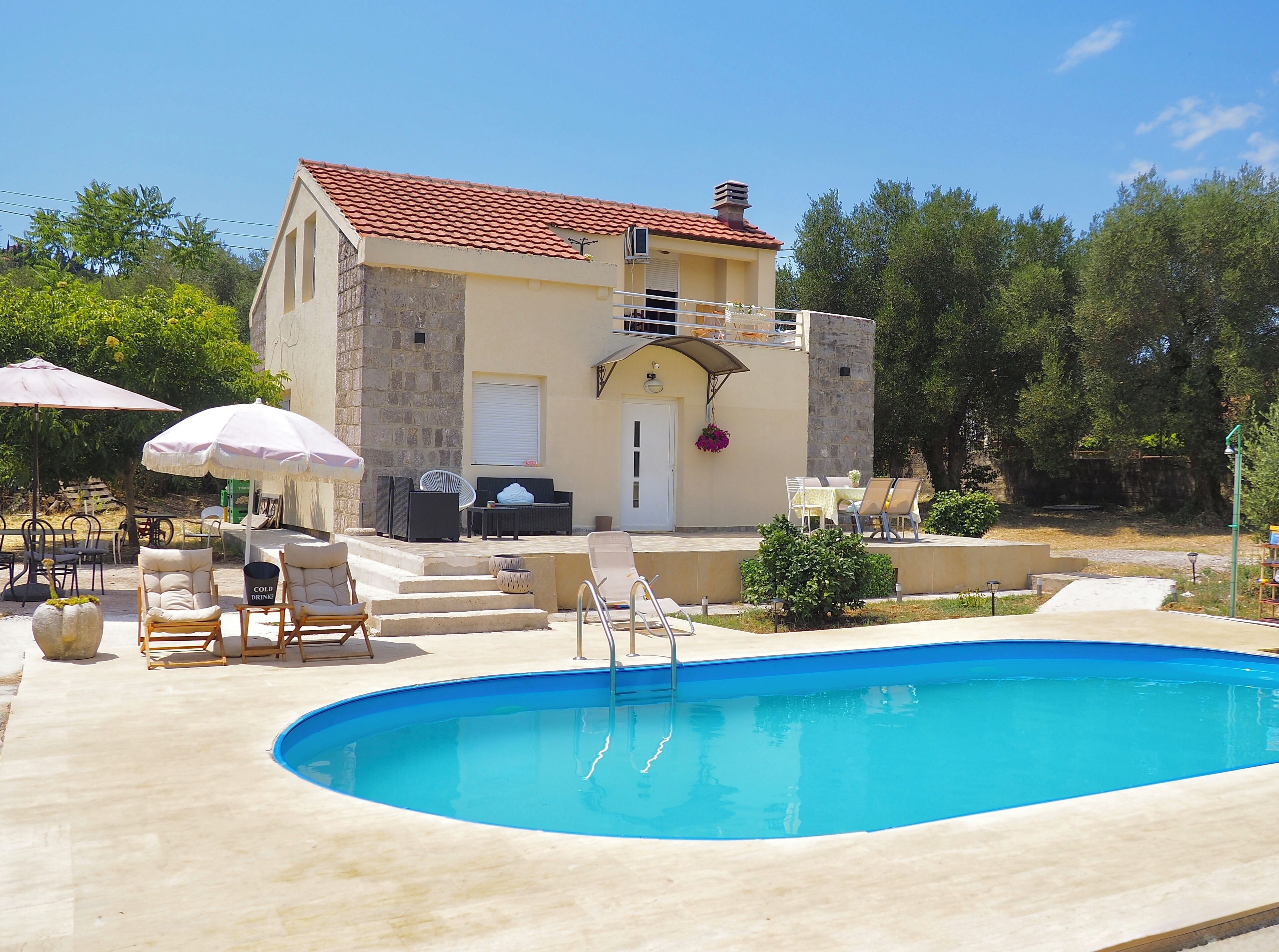 A poolside area with lounge chairs, umbrellas, and a stone building with a tiled roof.