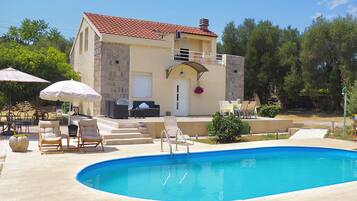 A poolside area with lounge chairs, umbrellas, and a stone building with a tiled roof.
