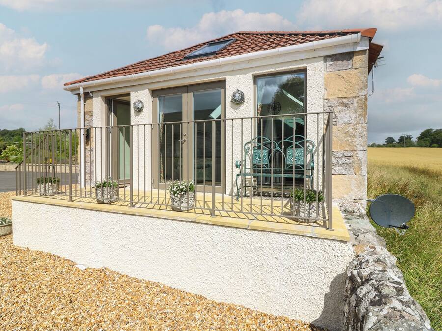A small stone building with a tiled roof, large windows, and a balcony with a metal railing.