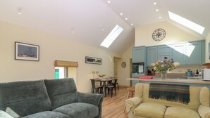 A spacious living area with a grey sofa, a yellow sofa, and a wooden coffee table. A dining area with a table and chairs is visible in the background.