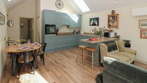 A modern kitchen with blue cabinets, a dining area with a wooden table and chairs, and a cozy living space with a sofa and a TV.