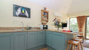 A kitchen with teal cabinets, a wooden countertop, a sink, a microwave, and a vase with flowers.