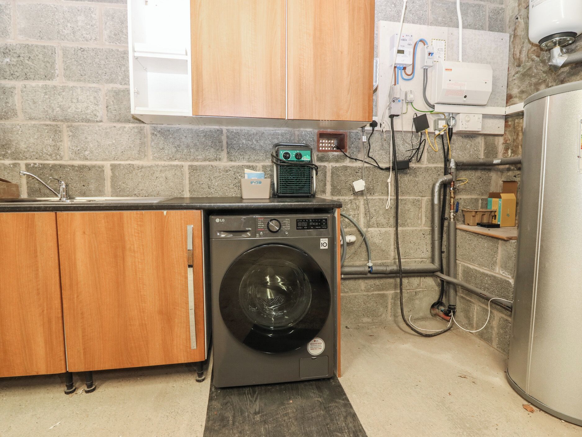 A laundry room with a front-loading washer and dryer, wooden cabinets, a tiled backsplash, and visible plumbing and electrical outlets.
