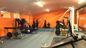 Et fitnesscenter med forskellig træningsudstyr, herunder styrkemaskiner og håndvægte.