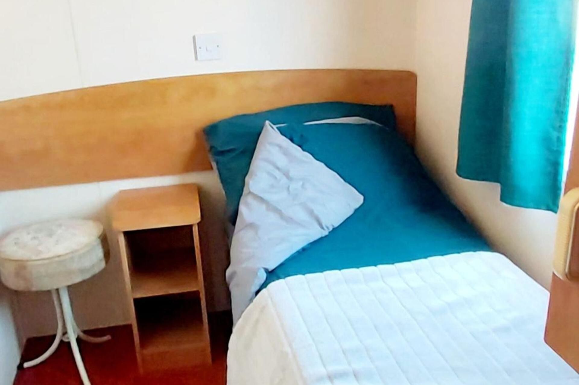 A single bed with a wooden headboard, a small bedside table, and a blue pillow.