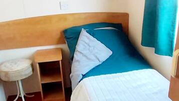 A single bed with a wooden headboard, a small bedside table, and a blue pillow.
