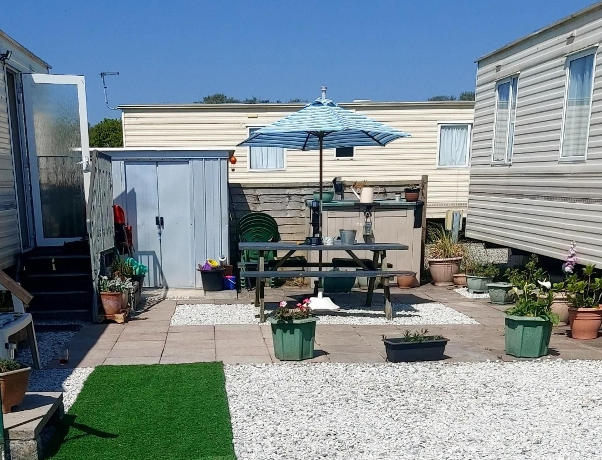 A patio area with a table, chairs, and an umbrella. There are potted plants and a small garden.