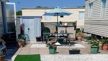 A patio area with a table, chairs, and an umbrella. There are potted plants and a small garden.