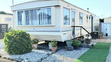 A mobile home with a front porch, potted plants, and a gravel driveway.