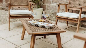 A stone wall patio with two wicker chairs and a wooden table with a tray of snacks and drinks. - Step into thoughtfully restored accommodation a stone's throw from Holy Island (Beal)