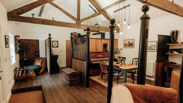A spacious room with high ceilings, exposed wooden beams, a piano, a dining table with chairs, and a large window providing natural light. - Step into thoughtfully restored accommodation a stone's throw from Holy Island (Beal)