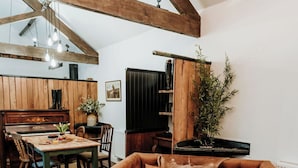 A rustic interior with exposed wooden beams, a wooden dining table with chairs, a sofa, and a radiator. - Step into thoughtfully restored accommodation a stone's throw from Holy Island (Beal)