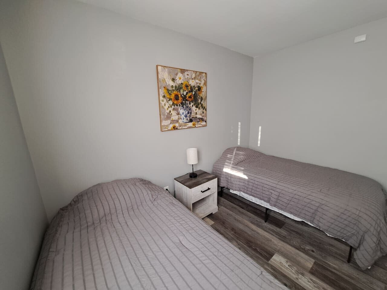 A bedroom with two beds, a nightstand with a lamp, and a painting on the wall.