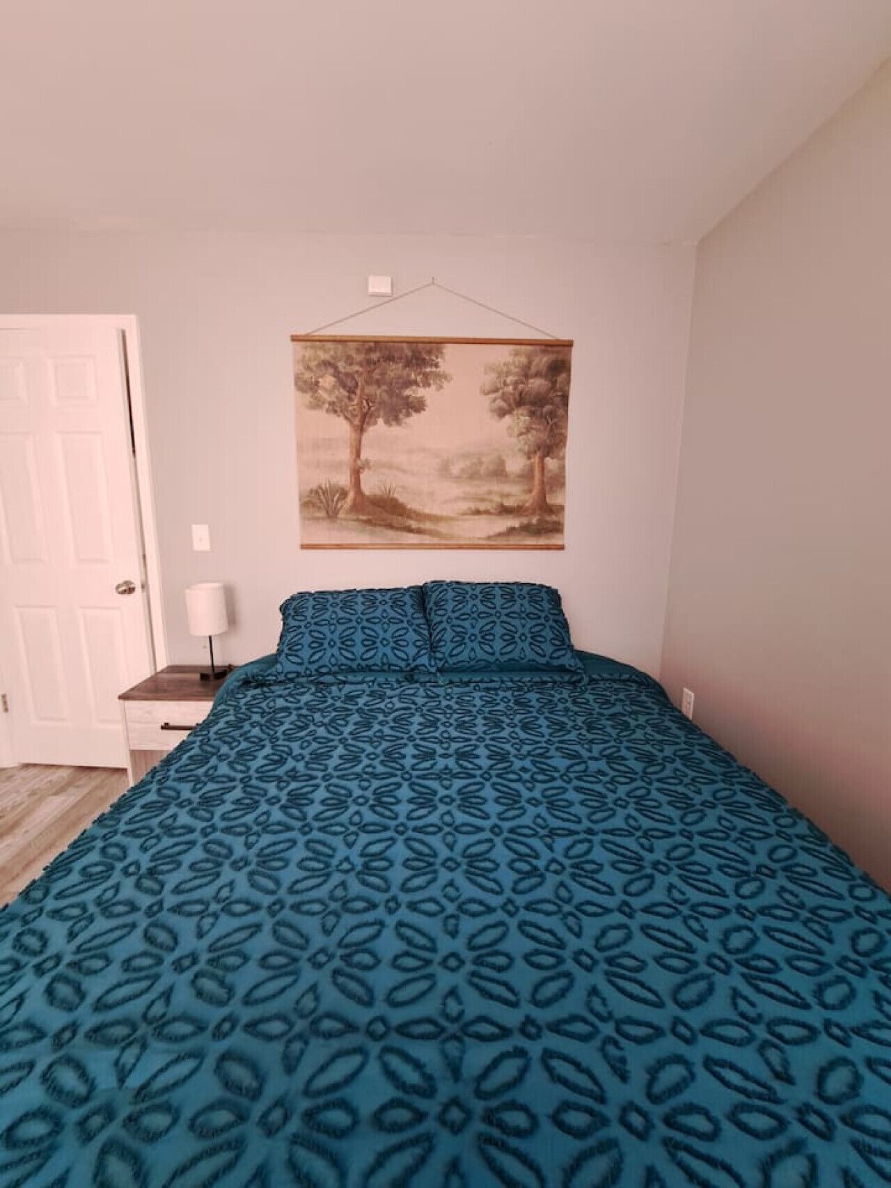Une chambre à coucher avec un lit, une table de chevet, une lampe et un tableau accroché au mur.