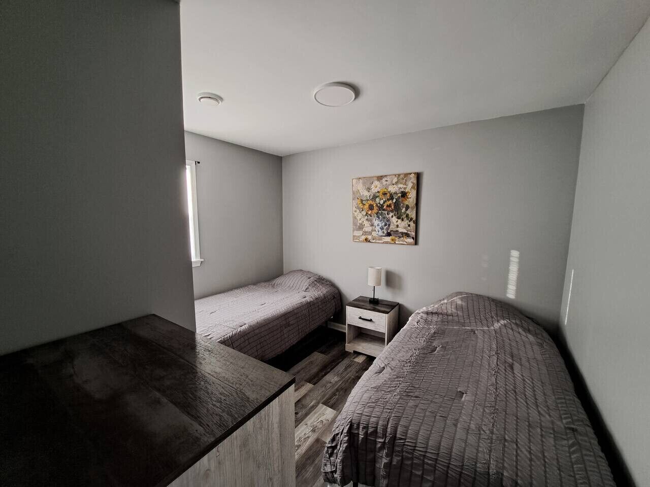 Een kleine, praktische kamer met twee eenpersoonsbedden, een nachtkastje en een schilderij aan de muur.