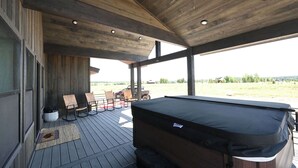 A covered outdoor area with a hot tub, wooden deck, and seating.