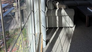Una sala de estar moderna con un ventanal grande, un sofá gris, una mesa de centro y un televisor montado en la pared.