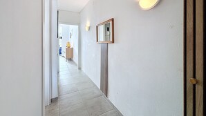A hallway with a tiled floor, a wooden door on the right, and a wall-mounted mirror. - GR CANAL 19 Roses / Roses - INTERimmo (Rosas / Roses)