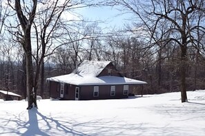 Une maison de plain-pied avec un toit à pignon, entourée d’un paysage enneigé et d’arbres sans feuilles.
