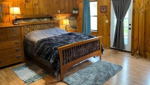 Een slaapkamer in een houten chalet met een bed, een dressoir en een stenen openhaard.