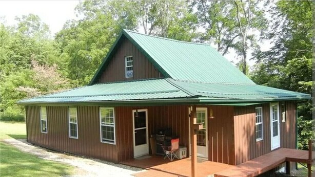 Een houten chalet met een groen dak, een veranda en een barbecueplek.