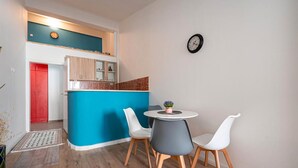 A compact living space with a kitchenette, a dining area with two chairs, and a small round table. - Central City Apartments – Walk to Everything! (Podgorica)