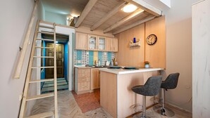 A compact kitchen with wooden cabinets, a tiled backsplash, and a small island with bar stools. - Central City Apartments – Walk to Everything! (Podgorica)
