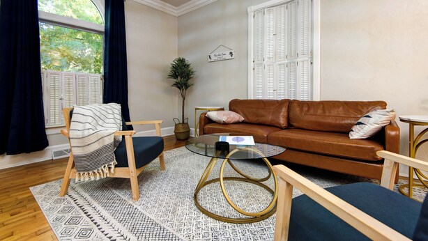A living room with a brown leather sofa, a glass coffee table, and a wooden armchair. - Charming & Cozy 3-bedroom house in wonderful Springfield with AC (Springfield)